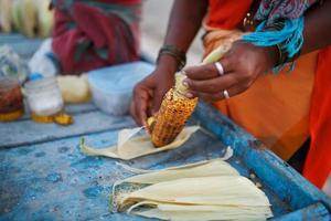 Close-up hands of a female street vendor are rubbing golden corn, grilled on coals, with lemon and spices photo