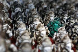 The stone statuette of Ganesh is green, contrasting with the group of light Ganesh on the counter of the Indian market photo