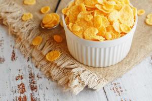 Bowl with golden flakes on a linen, on a light wooden table, next to a spoon. Rustic country style. View from above photo