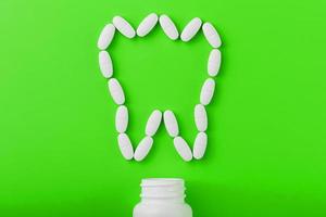 Calcium vitamin in the form of a tooth spilled out of a white jar on a Green background. photo