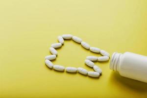 Calcium vitamin in the form of a tooth spilled out of a white jar on a yellow background. photo