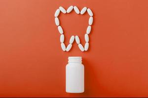 Calcium vitamin in the form of a tooth spilled out of a white jar on a red background. photo