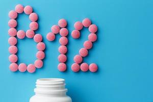 Pink pills in the shape of the letter B12 on a blue background, spilled out of a white can. photo