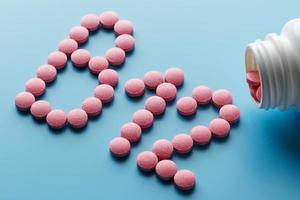 Pink pills in the shape of the letter B12 on a blue background, spilled out of a white can. photo