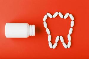 Calcium vitamin in the form of a tooth spilled out of a white jar on a red background. photo