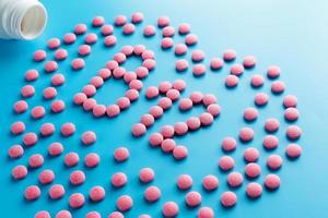 Pink tablets in the form of B12 in the heart on a blue background, spilled from a white can. photo