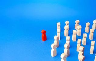 A figurine of a red man stands aside from the crowd of people. Stand out. Leadership qualities concept. Lead people with you. Be in the spotlight. Rejected from society, lonely. Speaker orator photo