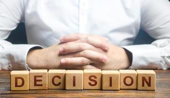 Man folded his hands on a background of blocks with the word Decision. Make the right decision, the answer to the question. Reasoning, weighing results and consequences. Authoritative opinion. photo