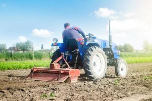 Farmer on a tractor with a milling machine processes loosens soil in the farm field. Preparation for new crop planting. Loosening surface, cultivating the land. Grind and mix soil on plantation. photo