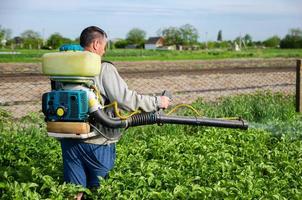 A farmer sprays chemicals on a potato plantation field. Control of use of chemicals growing food. Increased harvest. Protection of cultivated plants from insects and fungal infections. photo