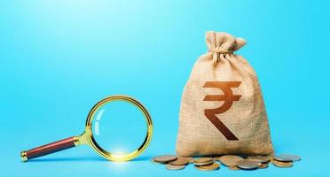 Indian rupee money bag and magnifying glass. Revising the budget to save money. Most favorable conditions for deposits. Origin of capital funds. Search for financing. Financial audit control. photo