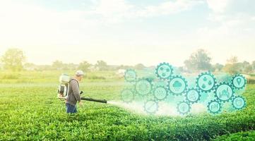 A farmer with a mist blower on potato plantation and technological innovation gears hologram. Using science and technology in agriculture to improve the efficiency and productivity of food production. photo