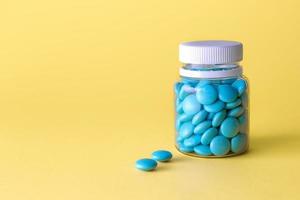 Medication bottle and blue pills on yellow background. photo