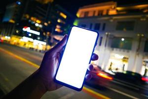 young man hand holding smart phone with empty screen at night photo