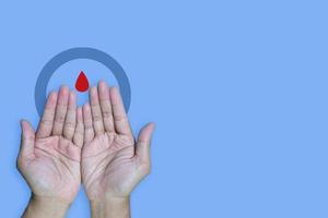 copyspace world diabetes day and hand gesture with red blood drop in man hands isolated on a blue background. 14 november photo