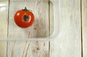 tomate rojo orgánico comido por orugas en mesa de madera foto