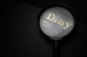 Showing DIARY Word Through Magnifying Glass. Isolated on black background. photo