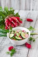 Fresh salad of cucumbers and radishes in a white bowl on the old wooden background photo