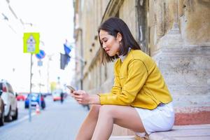 Smiling asian woman working on mobile smart phone while sitting on the floor Asian woman talking on mobile cellphone texting and surfing the net photo