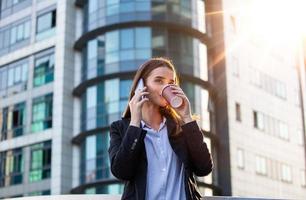 abogada empresaria profesional caminando al aire libre hablando por teléfono inteligente bebiendo café de un vaso de papel desechable. mujer de negocios en su teléfono móvil foto