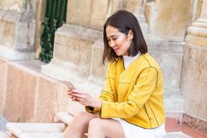 Smiling asian woman working on mobile smart phone while sitting on the floor Asian woman talking on mobile cellphone texting and surfing the net photo