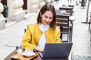 hermosa joven estudiante asiática que usa una computadora portátil mientras está sentada en una cafetería vintage. joven y bella chica que usa una computadora portátil personal para buscar información en Internet foto