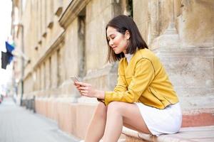 Smiling asian woman working on mobile smart phone while sitting on the floor Asian woman talking on mobile cellphone texting and surfing the net photo