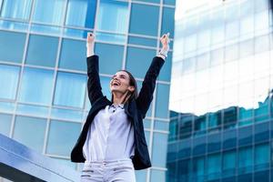 businesswoman in a business suit, exulted by happiness after finishing the deal, in the background skyscrapers. Concept of business, technology, economy and work and success photo