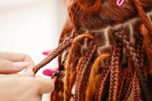 manos de peluquero trenzan rastas de jengibre de niña. foto