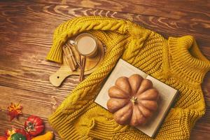 Round pumpkin, vintage book, cocoa and knitted sweater on wooden background. photo