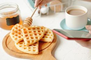Woman is having breakfast with waffles and coffee and chatting on phone. photo