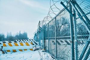 Barbed wire fence on border with concrete road blocks on ground in winter. photo