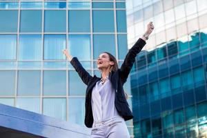 businesswoman in a business suit, exulted by happiness after finishing the deal, in the background skyscrapers. Concept of business, technology, economy and work and success photo