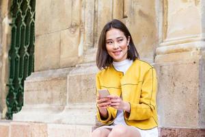 Smiling asian woman working on mobile smart phone while sitting on the floor Asian woman talking on mobile cellphone texting and surfing the net photo