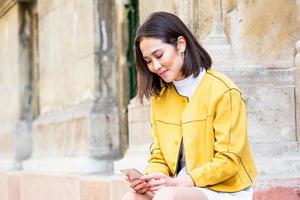 Smiling asian woman working on mobile smart phone while sitting on the floor Asian woman talking on mobile cellphone texting and surfing the net photo