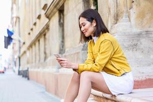 Smiling asian woman working on mobile smart phone while sitting on the floor Asian woman talking on mobile cellphone texting and surfing the net photo
