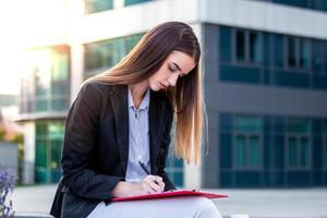 mujer de negocios ejecutiva con portapapeles contra el fondo urbano, firmando un contrato foto