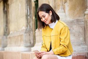 Smiling asian woman working on mobile smart phone while sitting on the floor Asian woman talking on mobile cellphone texting and surfing the net photo