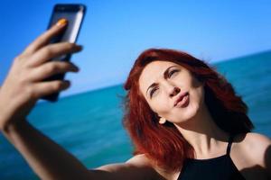 Mujer pelirroja toma selfie en la cámara del teléfono inteligente foto