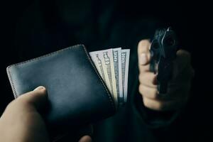 la mano del hombre le tiende una billetera de dinero al ladrón con un arma.