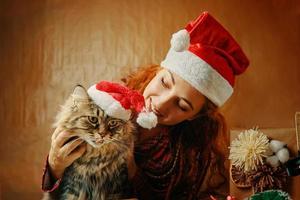 Woman in Santa Claus hat with cat in Christmas hat. photo