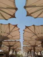 Medina, Saudi Arabia, 2022 - Umbrella construction on the square of Al-Masjid An-Nabawi or Prophet Muhammed Mosque are protecting people from sun at daytime and work as lights at night photo