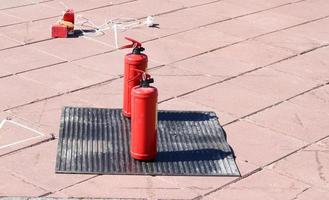 Two red metal large manual carbon dioxide or powder extinguishers for extinguishing a fire stand on a black rubber dielectric rug on the floor photo