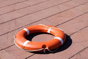 A large round orange plastic life ring for safety and rescue people in the water lies on the stone floor photo