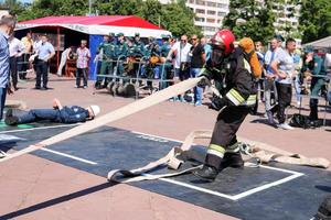 A fireman in a fireproof suit and a helmet running with an oxygen balloon pulling, holding a fire hose at a fire sport competition. Minsk, Belarus, 08.07.2018 photo