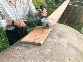 The man works with his hands, grinds the disk around for the grinder, the electric tool for grinding and polishing the surface of the wooden board photo