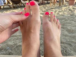 Female legs, feet with a beautiful red pedicure on the background of sand on vacation on the beach in a warm tropical eastern paradise country southern resort photo