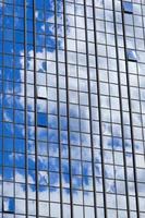 Texture of blue shiny glass skyscraper windows, buildings with reflection of white clouds and sky. The background