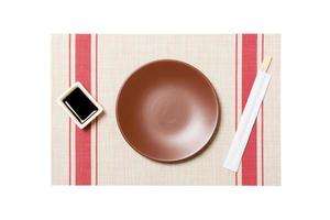 Empty round brown plate with chopsticks for sushi and soy sauce on sushi mat background. Top view with copy space for you design photo