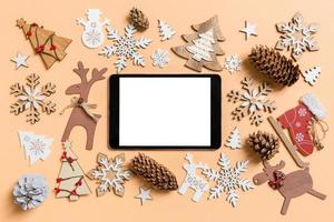 Top view of digital tablet surrounded with New Year toys and decorations on orange background. Christmas time concept photo
